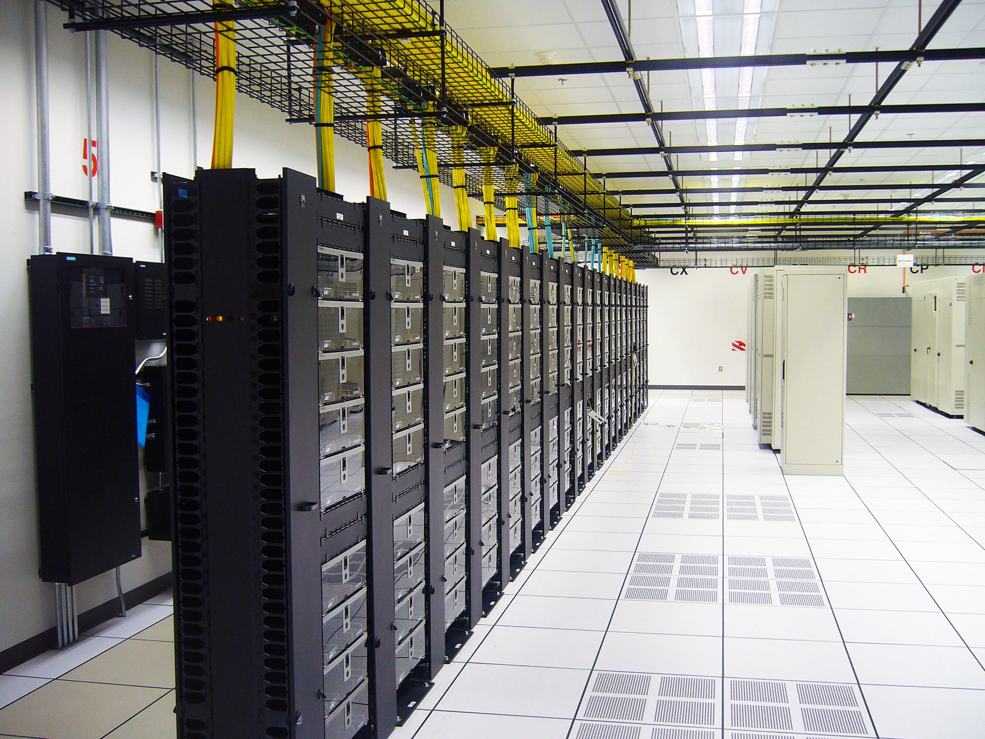 Conti Technology - Rows of black server racks in a data center with yellow network cables bundled above.